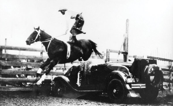 Roman-riding while jumping one of his signature Ford vehicles. Ted Elder jumping a vehicle while standing on one of his Irish Hunter horses; an extremely difficult feat. Photo courtesy Raymond Museum.