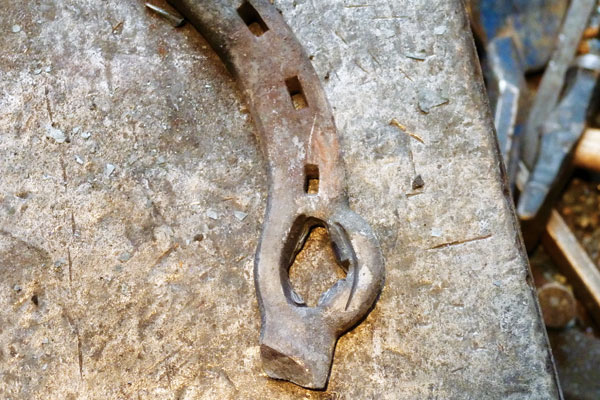 Using half a shoe, begin by splitting the shoe between two to three nail holes, depending on the width between them and the size of shoe. Slit the hole undersized by approximately ½?­-?¾ of the finished size, as the tab of metal left on the cut end will become part of the volume of metal in the ring, increasing its diameter. After slitting, clean up any ragged edges to prevent cold shuts that will weaken the opener's ring. Cold shuts are areas where two pieces of metal aren't fused together—in this case when a ragged edge folds over into the ring without welding to the parent metal, creating a thin point.   Begin to open up the split by hammering your slitting chisel deeper. Continue opening the ring with punches until it will fit onto the tip of your anvil horn or mandrel. If you don't have an anvil with a horn, you will need to make a mandrel to round the bottle opener. A simple mandrel is a 2-3 inch rod pointed on one end and held in a large vise.