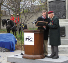 With mounted RCMP in red serge in the background, Ottawa Mayor Jim Watson hands over the Animals in War Proclamation to AIW leader Lloyd Swick, standing in front of the Boer War Monument. Photo by Shalindhi Perera.